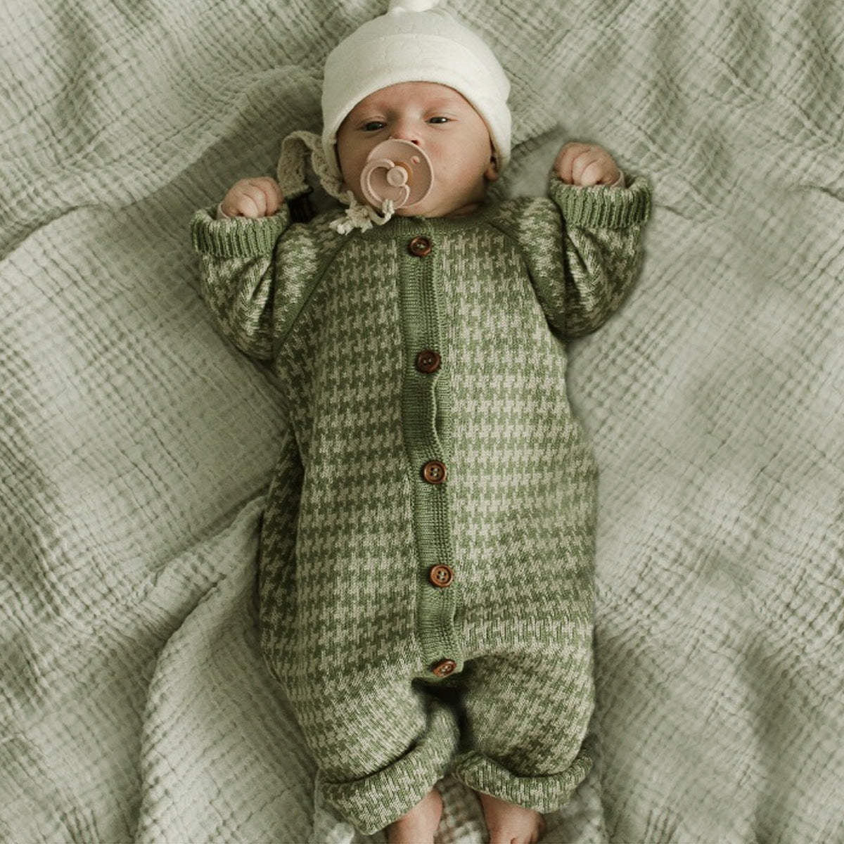Baby in a green knitted outfit lying on a textured blanket