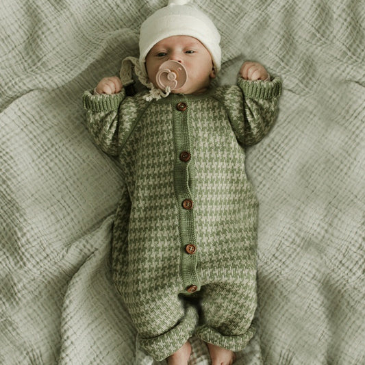Baby in a green knitted outfit lying on a textured blanket