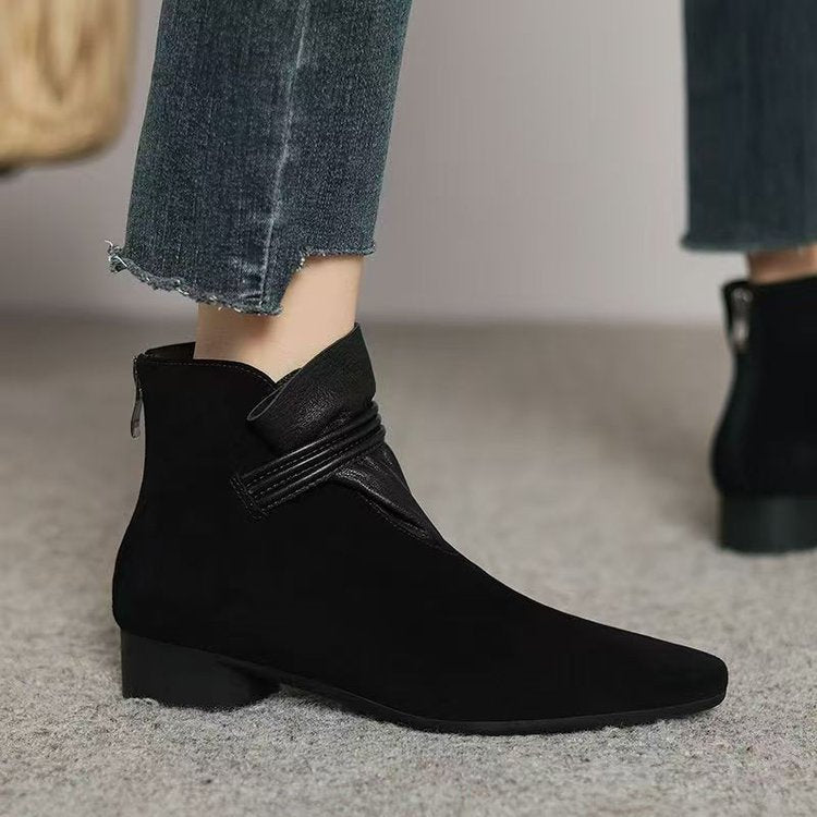 Black ankle boots worn with rolled-up jeans on a neutral background