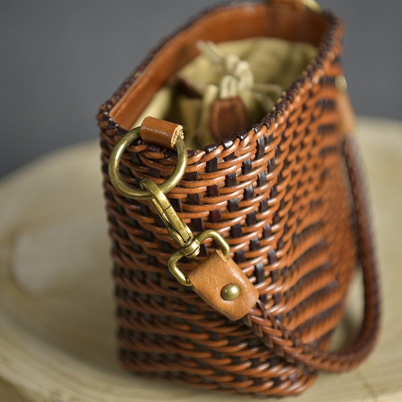 Brown woven handbag with leather strap and gold clasp on a neutral background