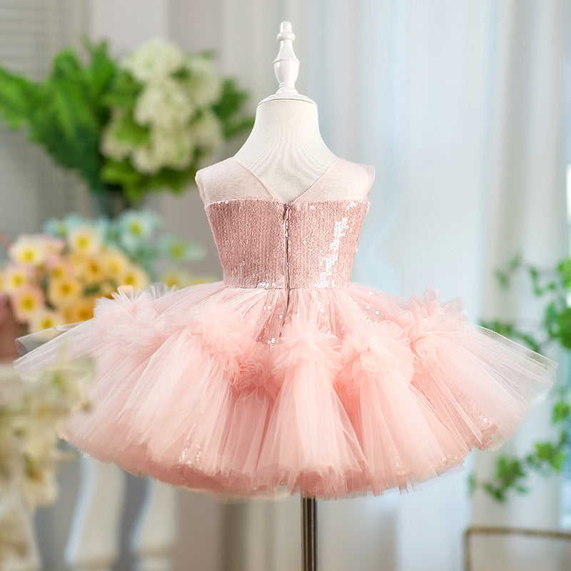 A light pink sequined and tulle tutu dress displayed on a white mannequin torso, with a softly blurred indoor floral background.