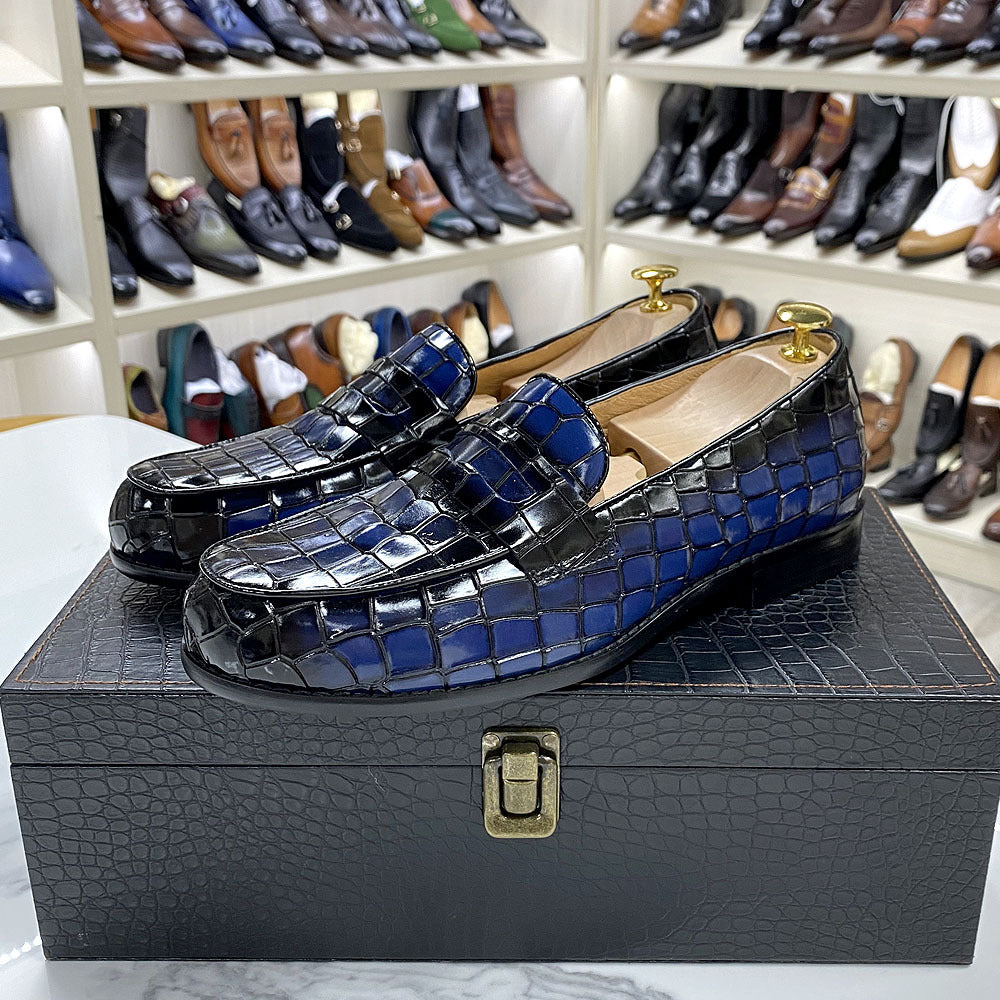 Blue and black patterned loafers on a black box with shelves of shoes in the background