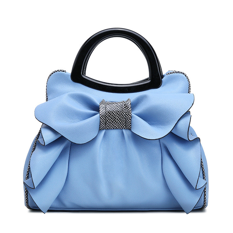 Blue handbag with a large bow and black handle on a white background
