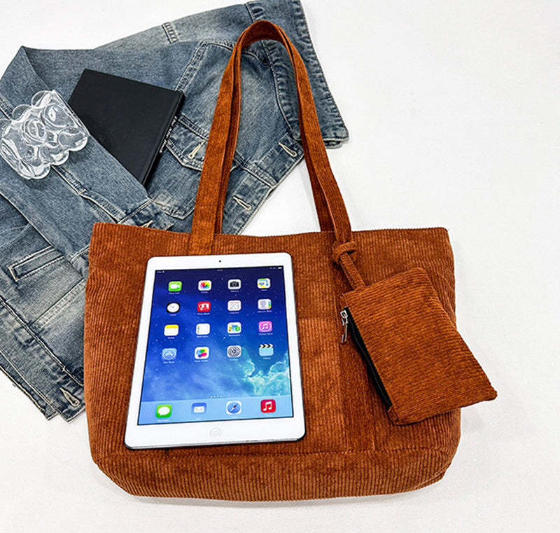 Brown tote bag with a tablet inside, denim jacket, and black phone on a white background