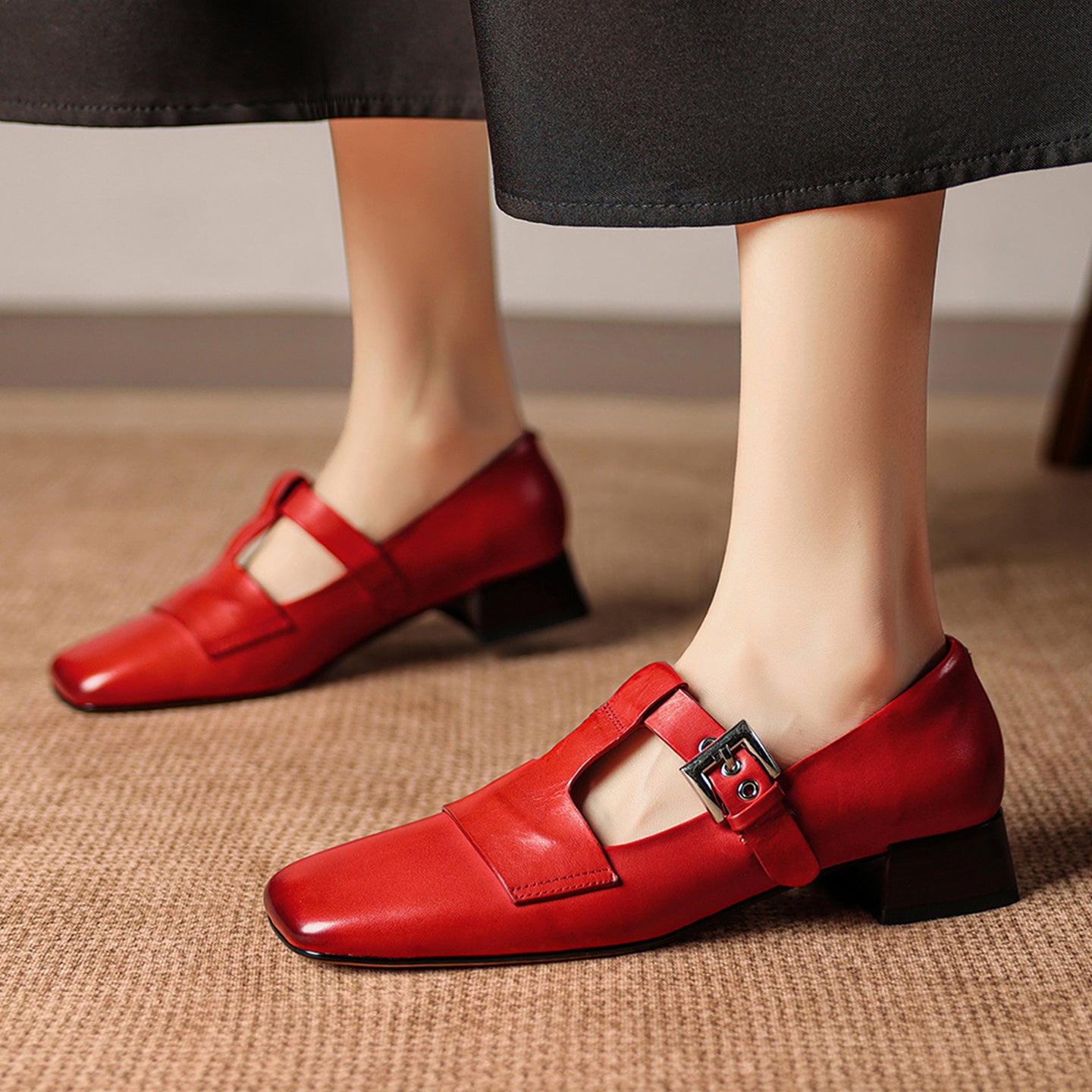 Red shoes with a buckle worn by a person on a beige carpet.