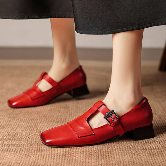 Red shoes with a buckle worn by a person on a beige carpet.