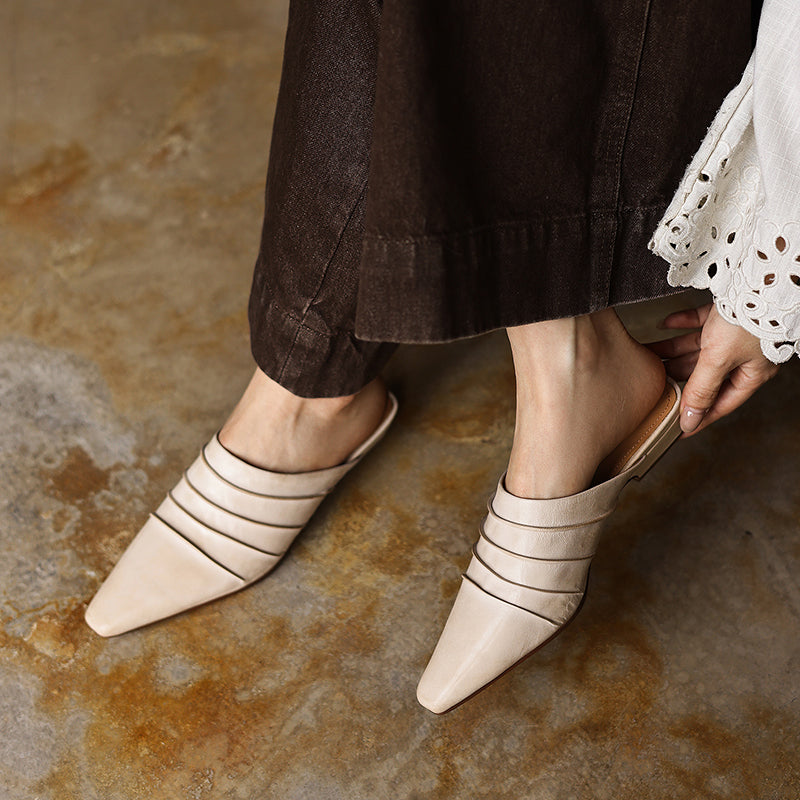 Beige strappy mules worn with brown pants on a stone floor.