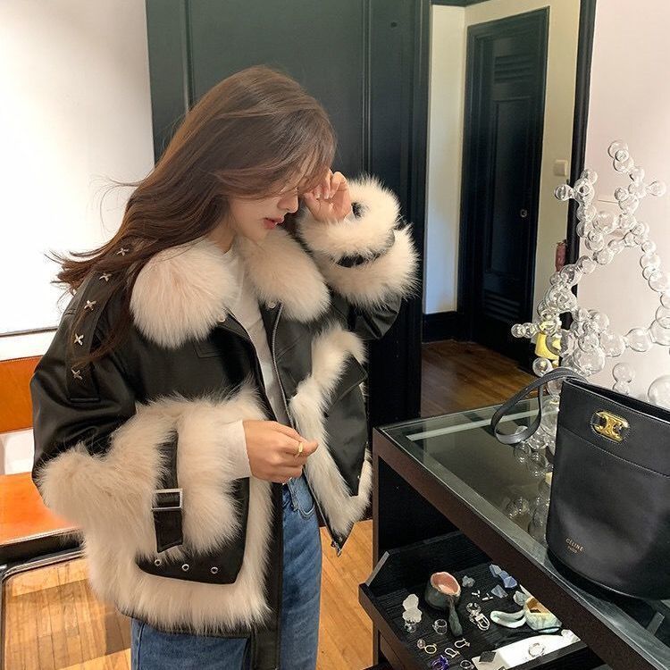 Woman wearing a fur-trimmed coat in a room with a mirror and jewelry.