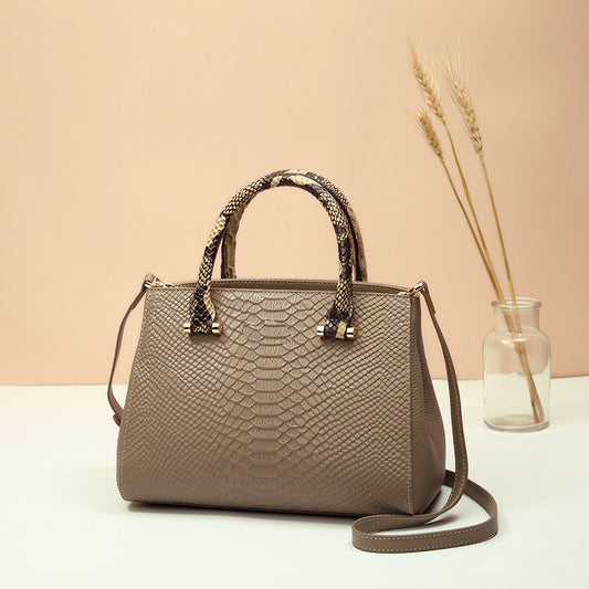 Brown textured handbag with snake skin pattern on handle against a beige background