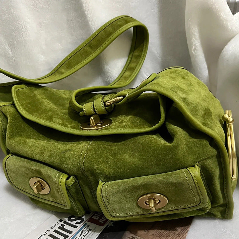 Green suede handbag with gold accents on a white surface