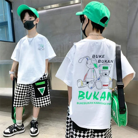Two children wearing matching outfits with a green cap, white t-shirt, and black and white checkered shorts.