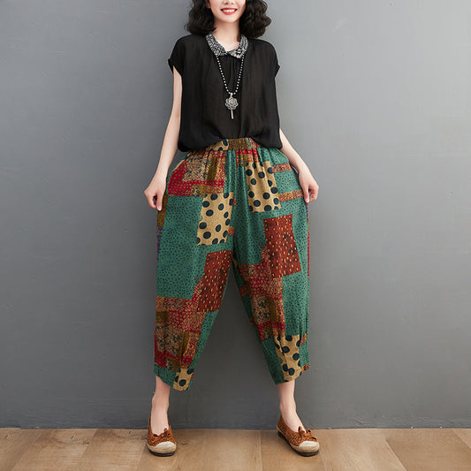 Woman wearing a black top and colorful patchwork pants against a gray wall.