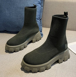 Black ankle boots with thick soles on a light gray surface