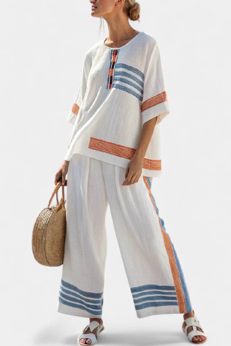 Woman wearing a white outfit with blue and orange stripes, holding a straw bag on a light background