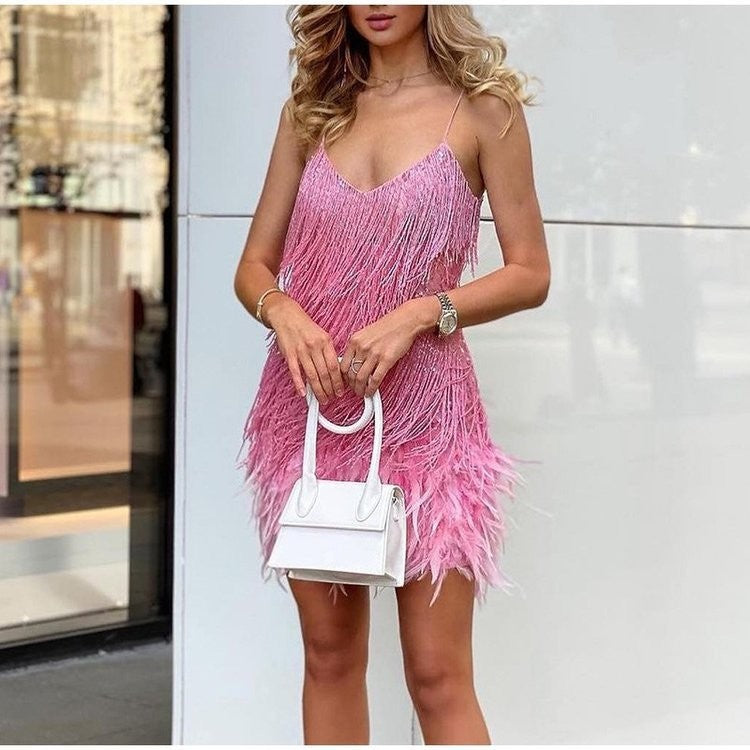 Woman wearing a pink fringe dress holding a white handbag against a light background