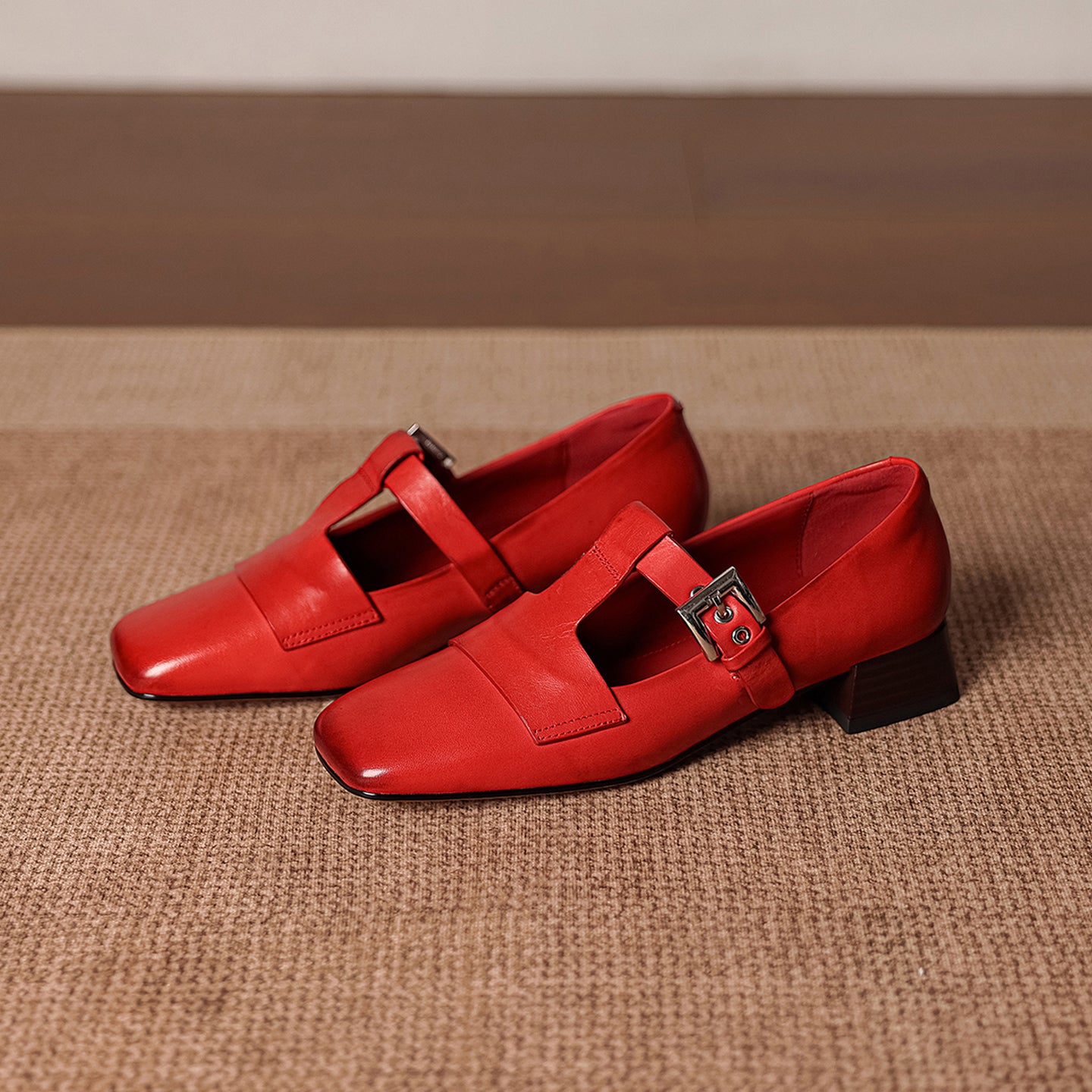 Pair of red shoes with buckles on a textured brown surface
