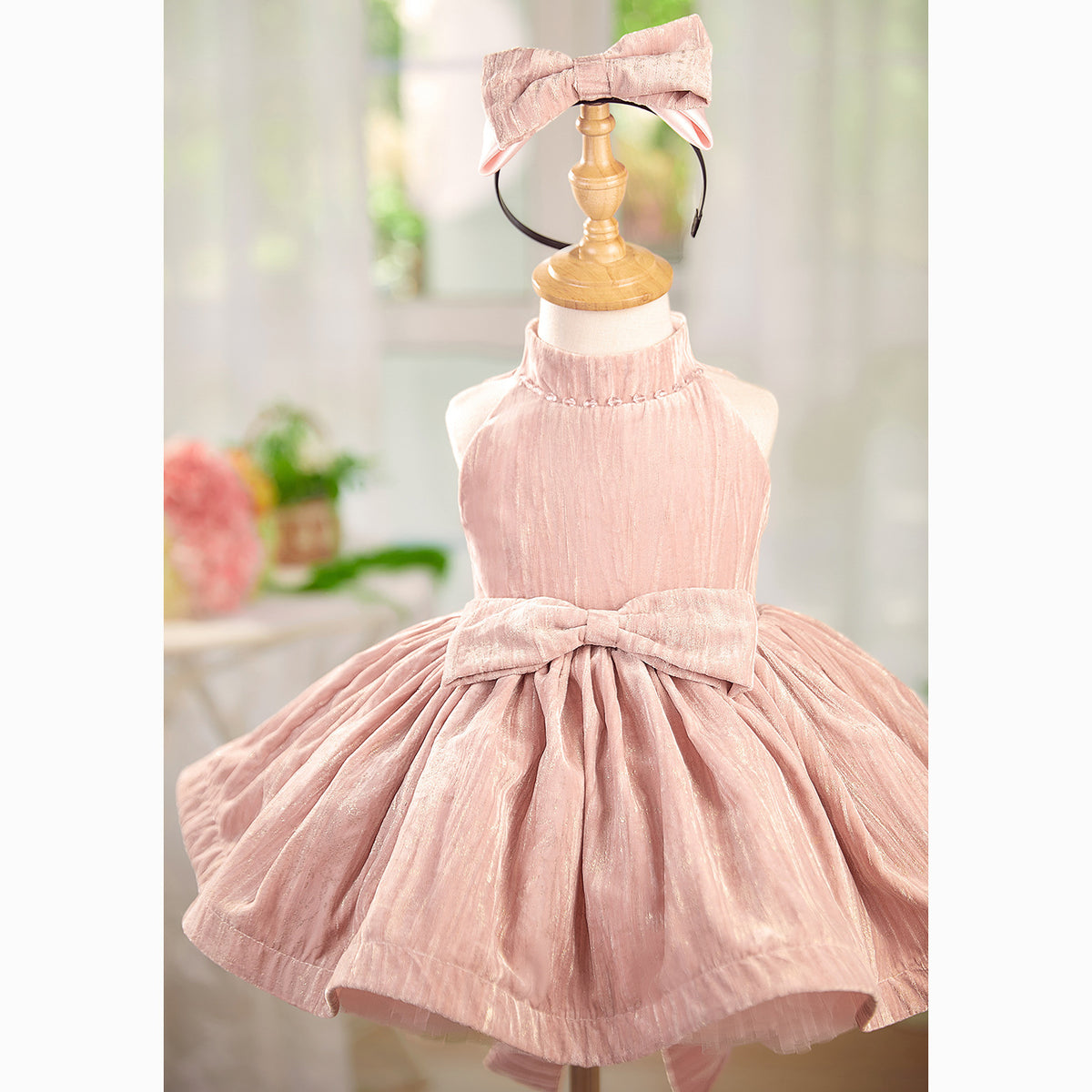Pink children's dress with a bow on a mannequin against a blurred indoor background