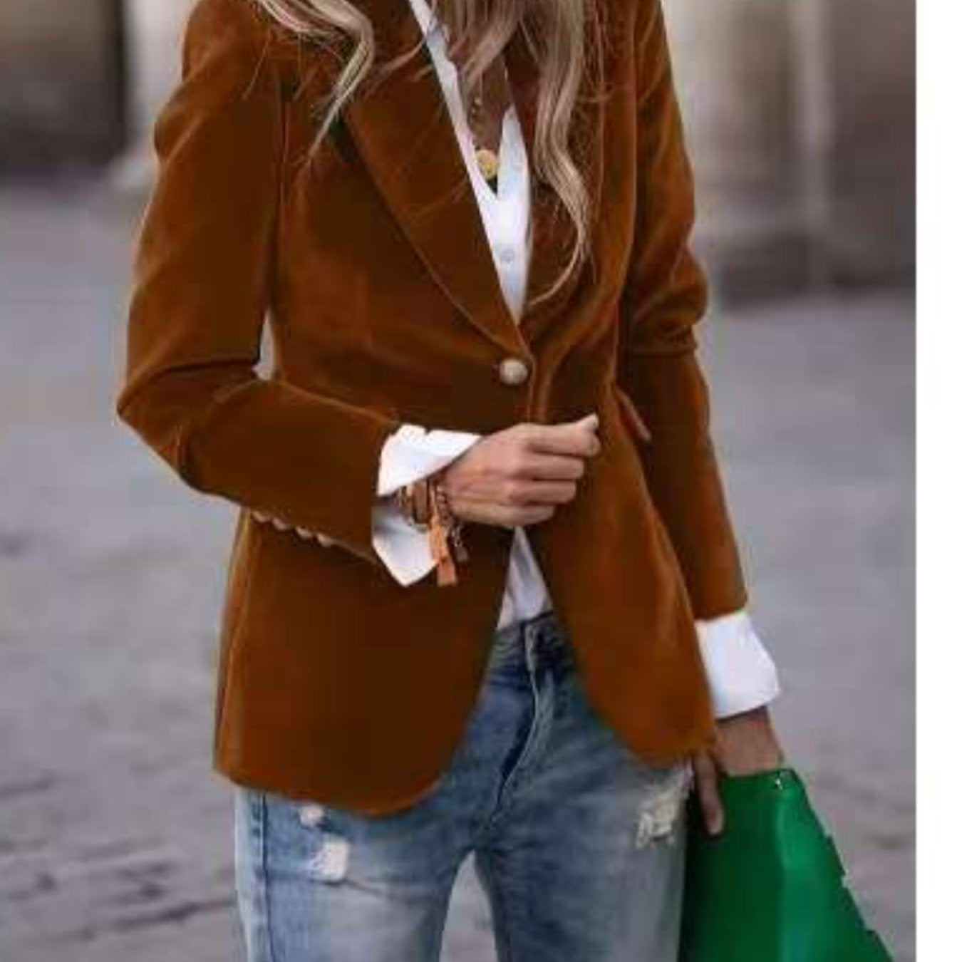 Person wearing a brown blazer over a white shirt with blue jeans, holding a green bag.