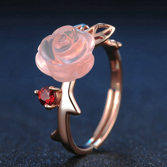 Rose gold ring with a pink rose and red gemstone on a dark blue background