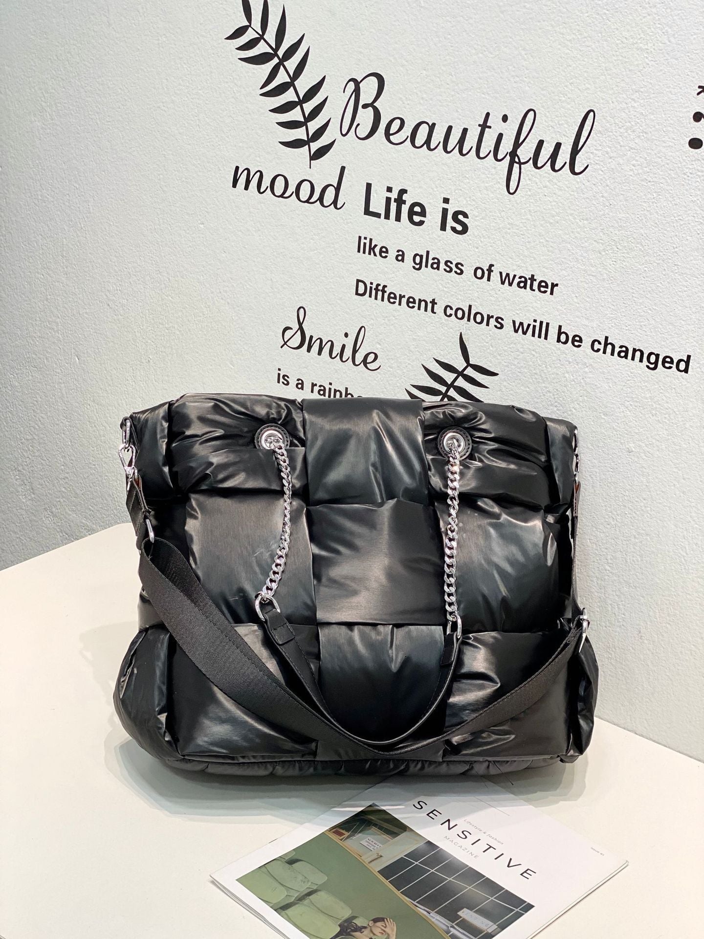 Black quilted handbag with chain details on a white surface with motivational text in the background.