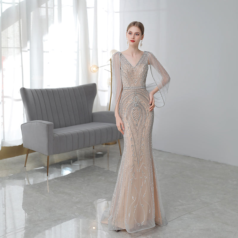 Woman in a beaded evening gown standing in a modern room with a gray sofa.