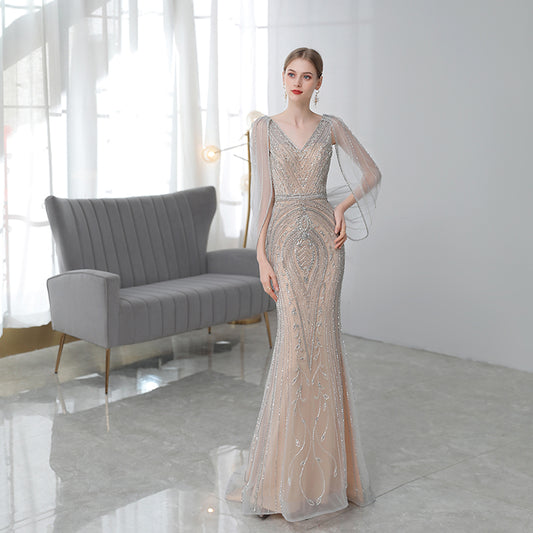 Woman in a beaded evening gown standing in a modern room with a gray sofa.