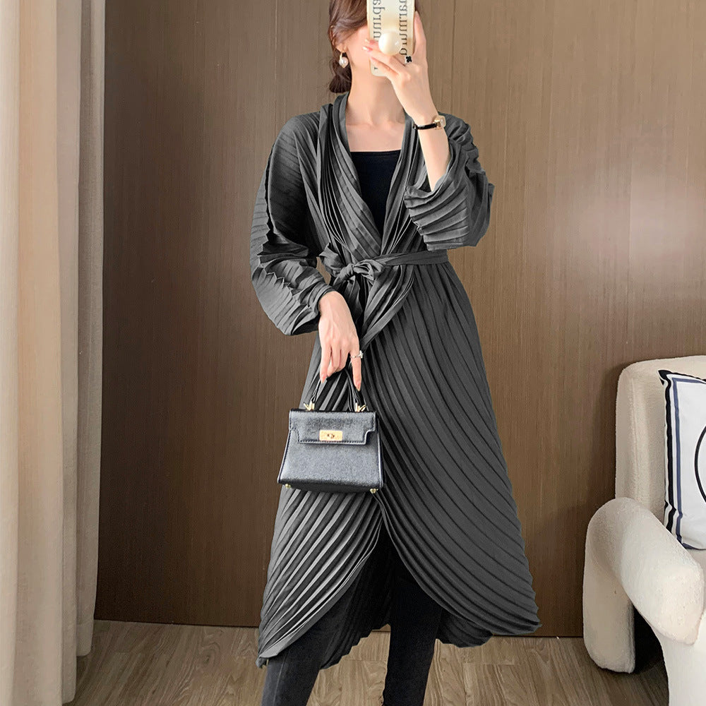 Woman wearing a gray pleated dress holding a matching handbag indoors.