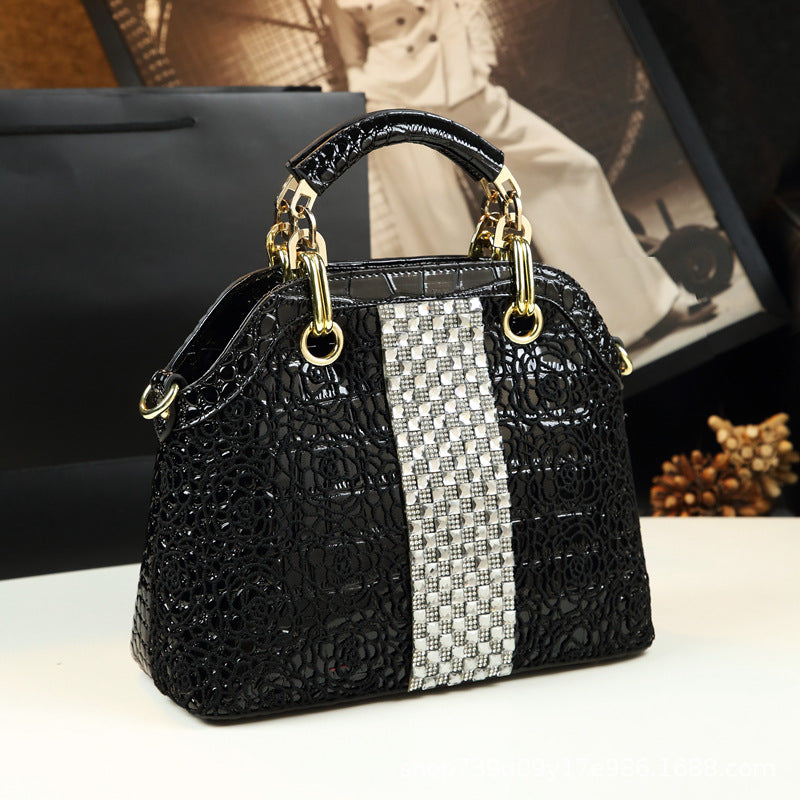 Black textured handbag with a silver woven strap on a white surface.