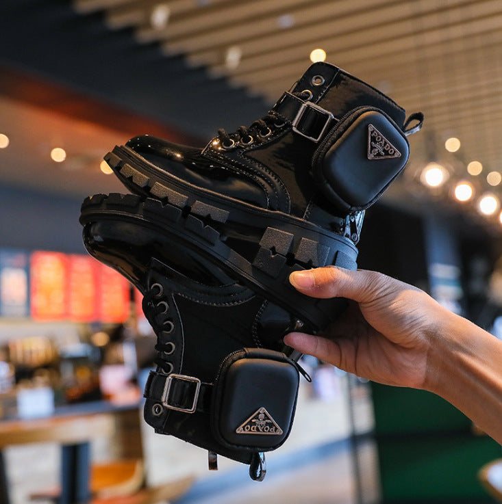 Black boots with a brand logo held by a hand in an indoor setting