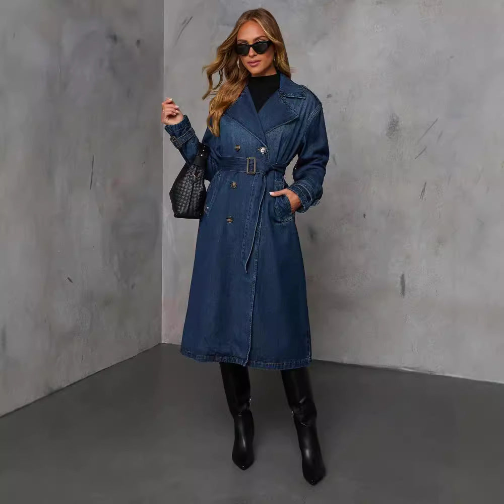Woman wearing a blue trench coat against a gray concrete wall.