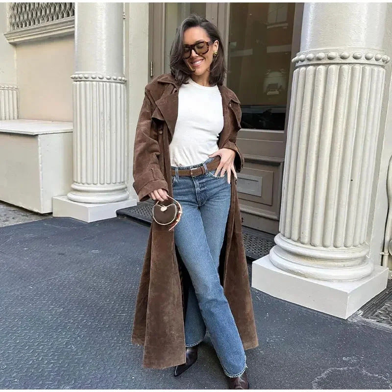 Woman in a brown coat and blue jeans standing in front of classical columns. By Millivan 