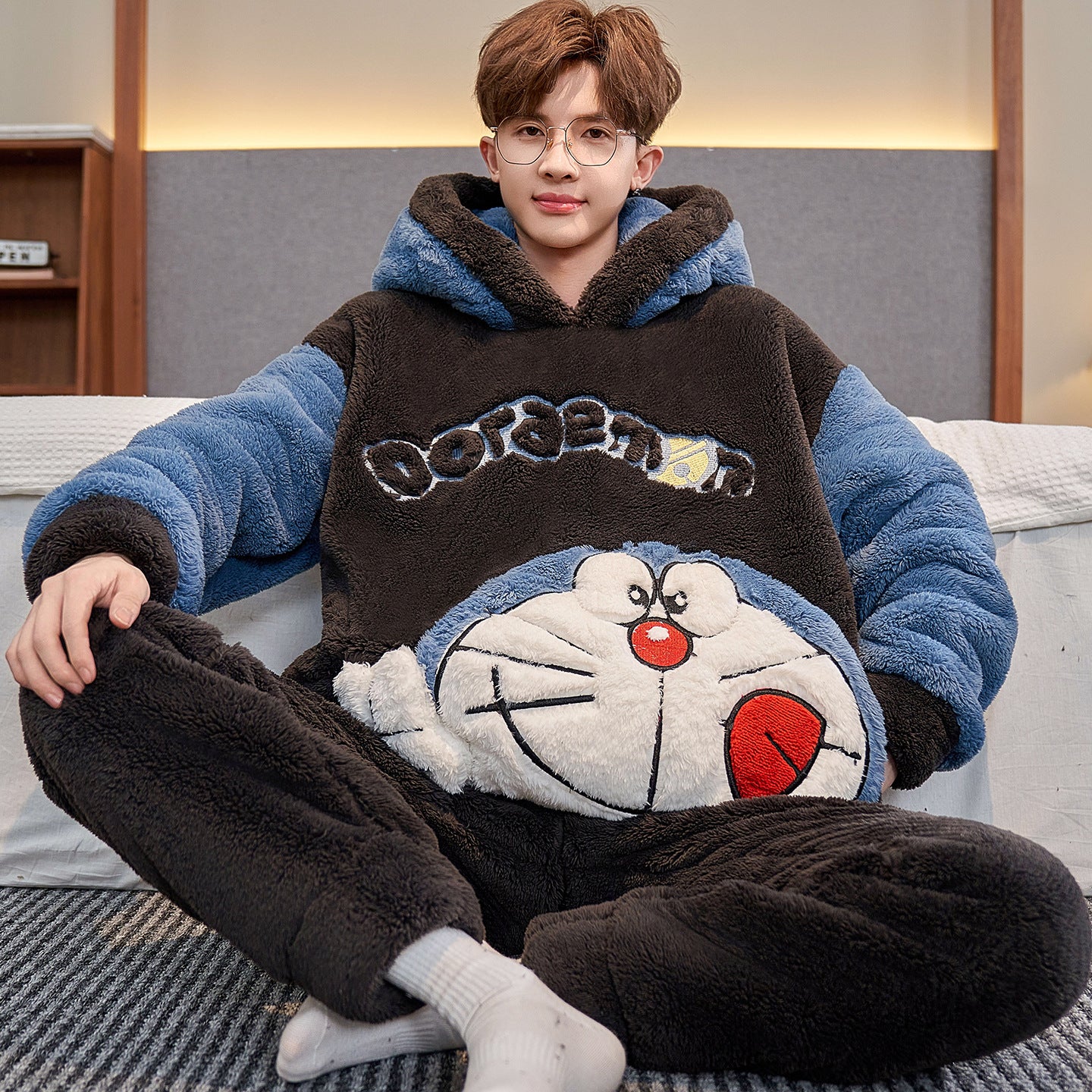 Person wearing a Doraemon-themed onesie sitting on a bed.