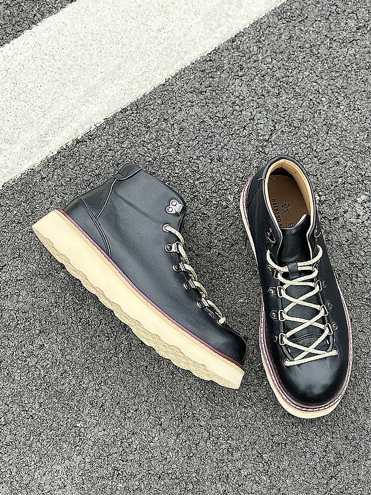 Pair of black leather boots with white soles on a gray pavement.
