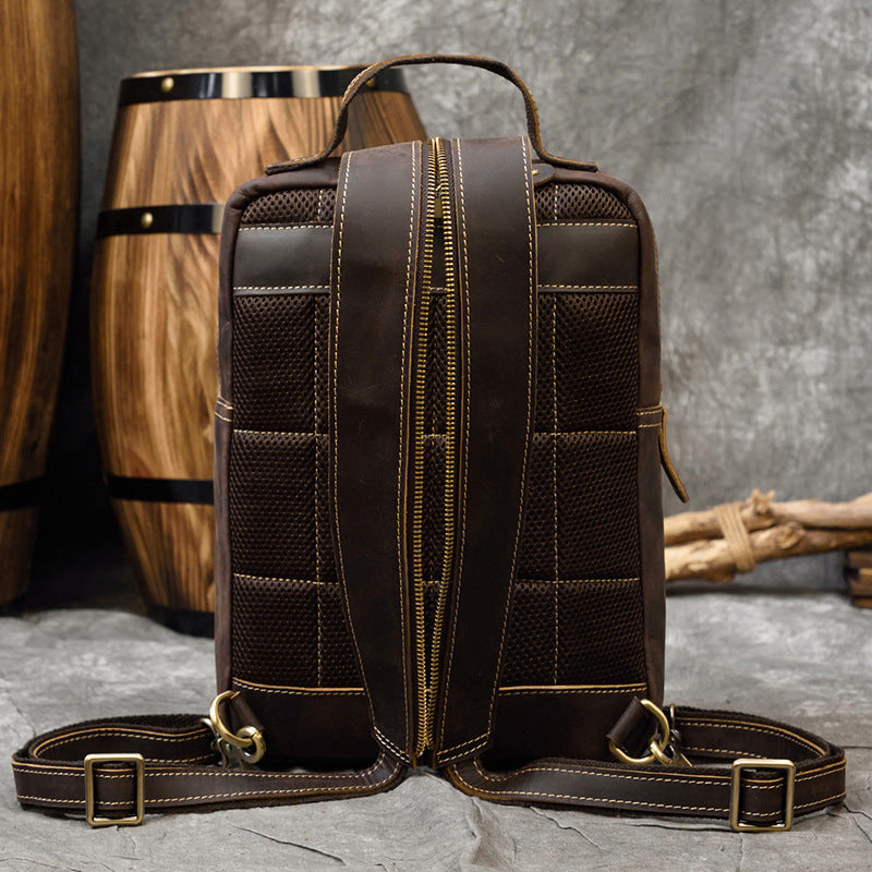 Brown leather backpack with gold zippers on a textured surface with wooden barrel in the background