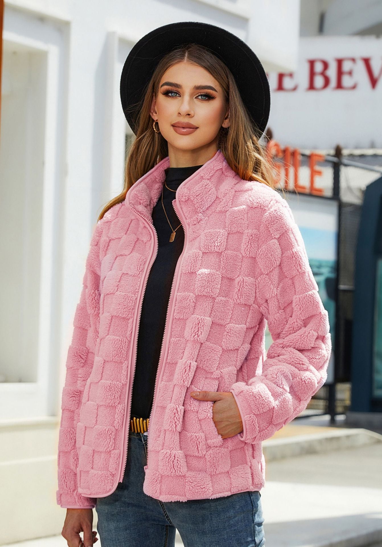 Woman wearing a pink quilted jacket and black hat outdoors.
