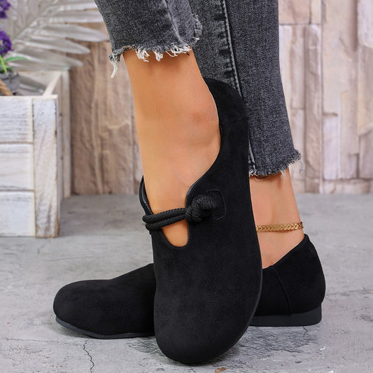 Black suede shoes worn with gray jeans on a stone surface.