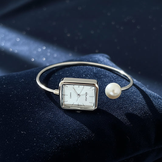 Silver bracelet with a square watch face and pearl accent on a gray surface