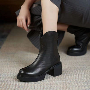Black leather ankle boot worn by a person on a textured floor.