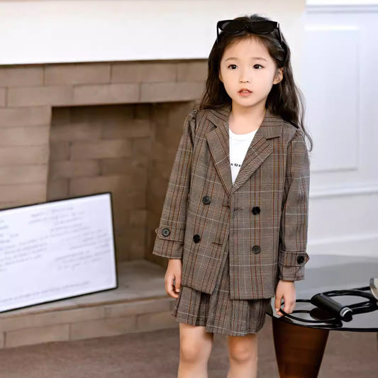 Young girl wearing a plaid suit standing in a room with a fireplace.