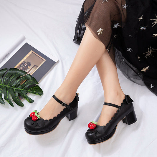Black shoes with strawberry decorations worn by a person on a white background