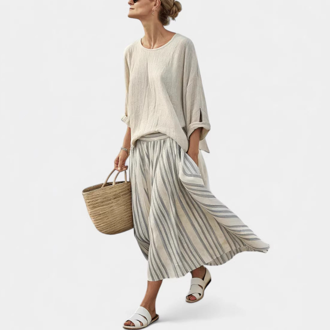 Woman wearing a beige top and striped skirt, holding a woven bag on a white background
