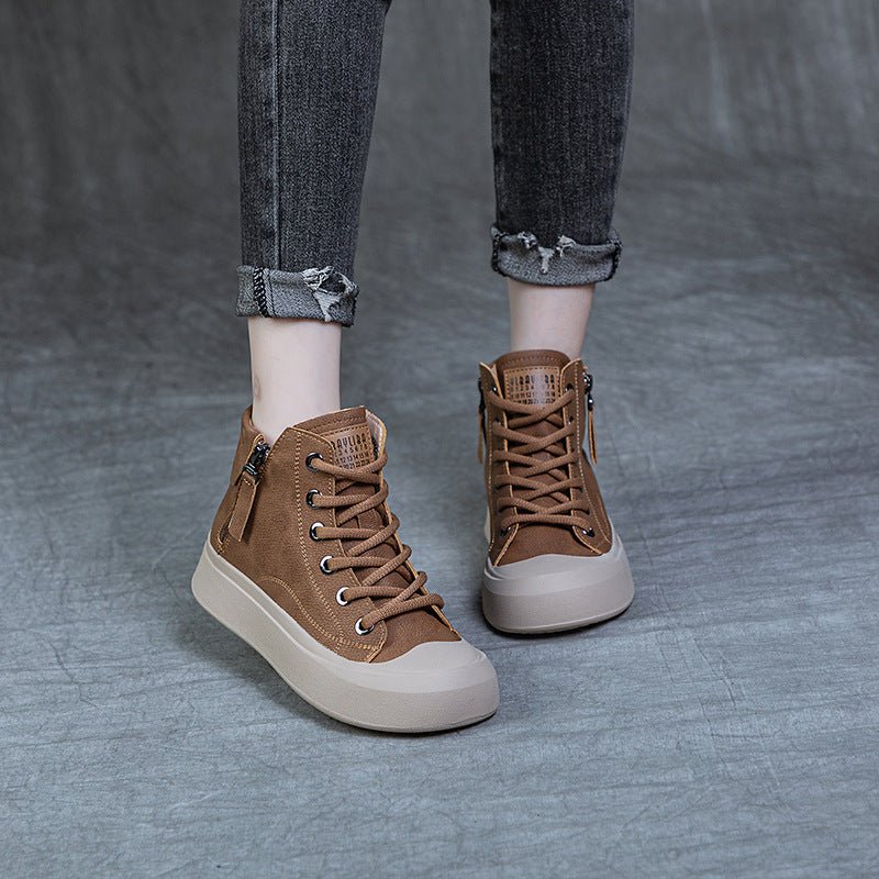 A person wearing brown lace-up high-top sneakers with side zippers and off-white rubber soles, paired with cuffed gray jeans, standing on a textured gray floor.