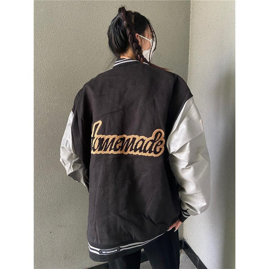 Person wearing a black and white jacket with 'Homemade' text on the back against a plain wall.