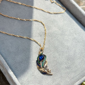 Gold necklace with a blue gemstone pendant on a light gray surface