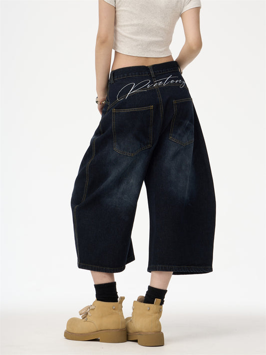 Person wearing dark blue wide-leg jeans with 'Rochester' branding, beige boots, and a white crop top on a white background.