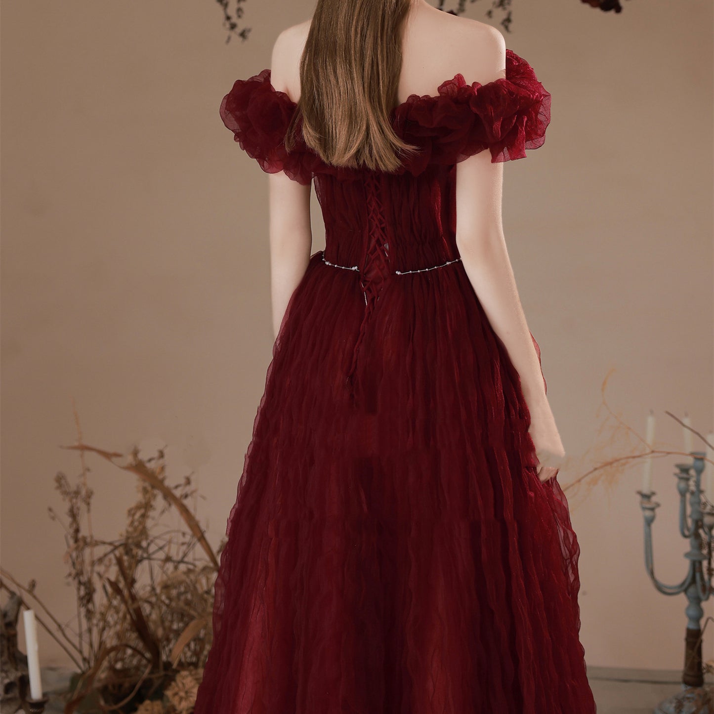 Woman wearing a burgundy evening gown with floral details in an indoor setting.
