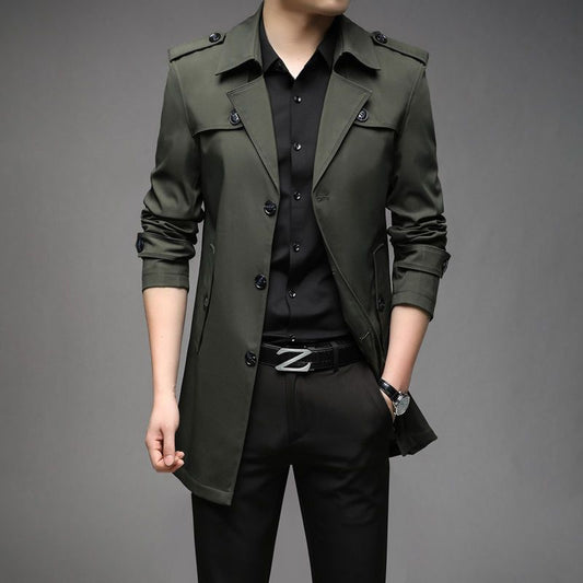 Person wearing a green trench coat over a black shirt and pants on a gray background