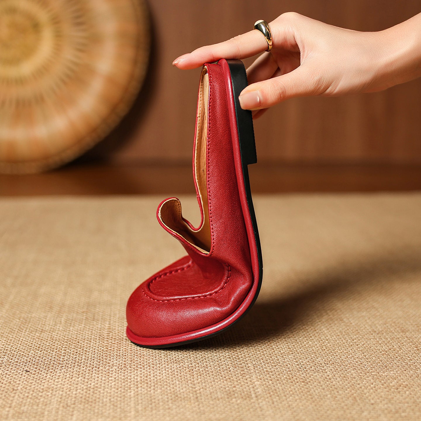 Red leather shoe with a unique design held by a hand on a beige surface.