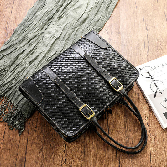 Black woven handbag with gold buckles on a wooden surface with a scarf and book in the background