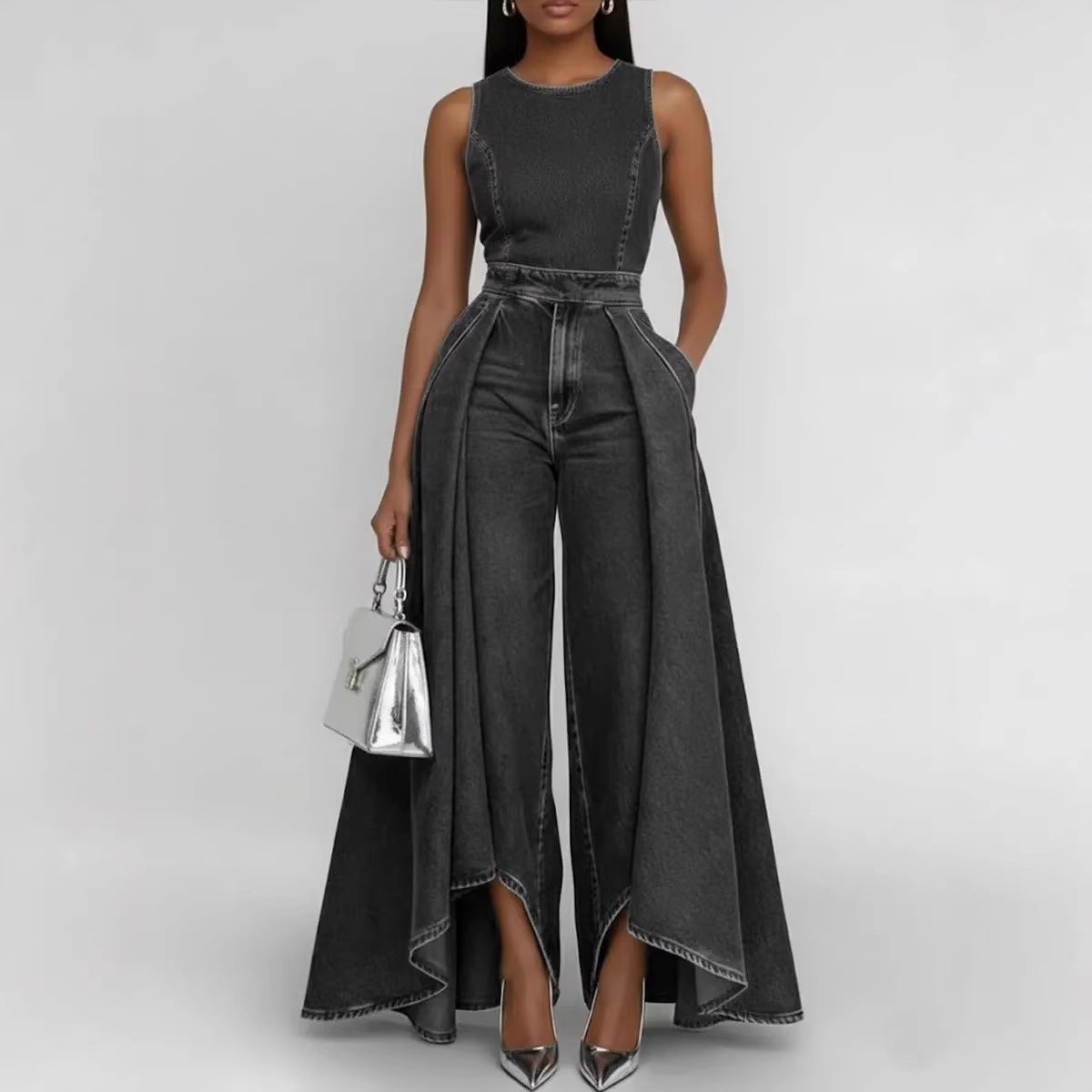 Woman wearing a black denim jumpsuit with a silver handbag on a light gray background